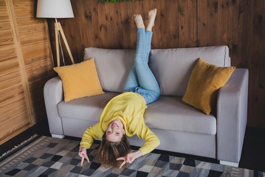 Full body photo of nice young woman lying sofa upside down v-sign wear stylish yellow sweater modern light cozy interior flat indoors