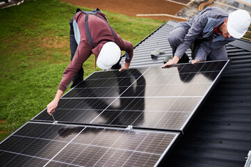 Installers installing photovoltaic solar panels on roof of house. Men engineers in helmets building...