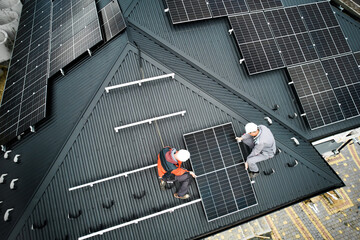 Installers building photovoltaic solar module station on roof of house. Men electricians in helmets...