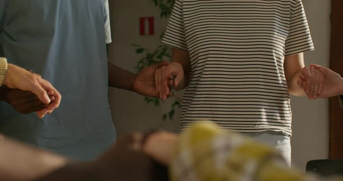 Young people of different nationalities hold hands when they pray, standing in a circle. Close-up of their hands, unrecognizable persons