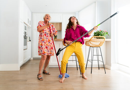 Beautiful grandmother and granddaughter together at home cleaning apartment and dancing & singing - Cheerful granma and nephew spending quality time together