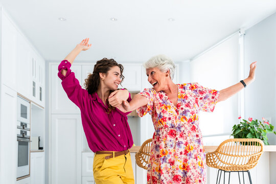 Beautiful grandmother and granddaughter together at home dancing and having fun - Cheerful granma and nephew spending quality time together - Powered by Adobe