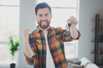 Photo of attractive young male winning hold house key wear checkered shirt cozy day light home interior living room