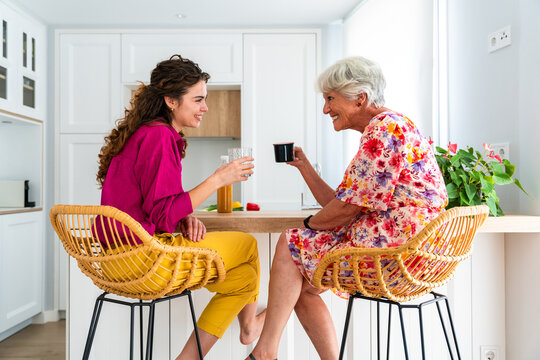 Beautiful grandmother and granddaughter together at home talking while having coffee - Cheerful granma and nephew spending quality time together