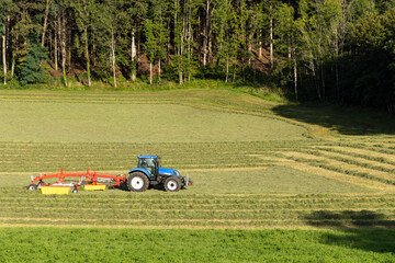 Tractor turning hay in spring meadow, Jura, France