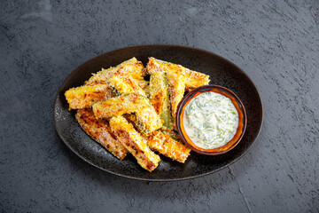 Healthy zucchini fries with yogurt and herbs sauce on dark background with copy space