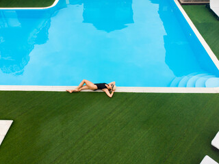 Aerial drone view of woman relaxing near pool in hotel. lyign on the edge of pool Summer holidays, enjoying summer vacations. Copyspace, space for text