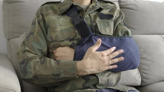 Close up of a disabled soldier grabbing his painful bandaged arm on a couch at home