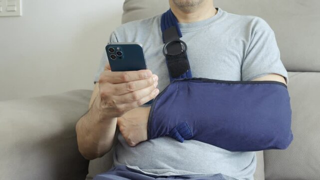 Close up of man hands with broken arm wearing sling using smart phone at home