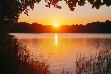 This photograph beautifully captures the sun setting over a lake, casting a golden reflection on the water and illuminating the surrounding nature with warm hues.