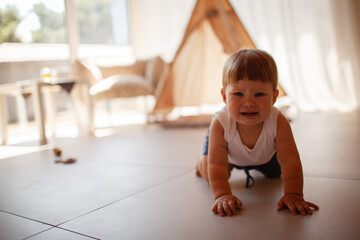 Small child under one year old plays in the room against the backdrop of wigwam in beige shades. The infant baby is happy and dressed  bodysuit. The cozy home environment © Вероника Зеленина