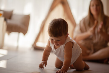Small child under one year old plays in the room with mom against the backdrop of wigwam in beige shades. The infant baby is happy and dressed  bodysuit. The cozy home environment © Вероника Зеленина
