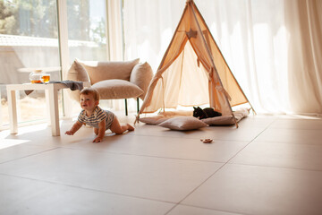 Small child under one year old plays in the room against the backdrop of wigwam in beige shades. The infant baby is happy and dressed  bodysuit. The cozy home environment © Вероника Зеленина