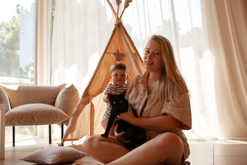 Small child under one year old plays in the room with mom against the backdrop of wigwam in beige shades. The infant baby is happy and dressed  bodysuit. The cozy home environment © Вероника Зеленина