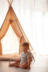 Small child under one year old plays in the room against the backdrop of wigwam in beige shades. The infant baby is happy and dressed  bodysuit. The cozy home environment © Вероника Зеленина