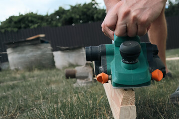 A carpenter planes a piece of wood using an electric plane. Carpenter is planing a wooden plank