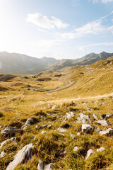 Golden sunlight illuminates a vast mountain landscape with rolling hills and rocky outcrops in sunset 