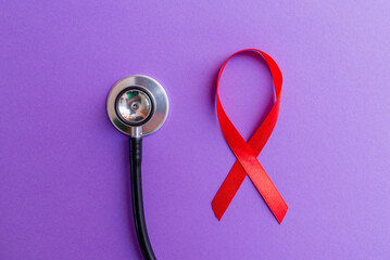 Red ribbon, stethoscope on the purple background. Woman breast cancer concept. Top view.