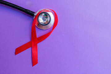 Red ribbon, stethoscope on the purple background. Woman breast cancer concept. Top view, copy space.