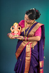 Happy traditional Indian woman wearing saree holding and posing with Ganesha statue on the occasion...