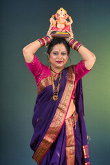 Happy traditional Indian woman wearing saree holding and posing with Ganesha statue on the occasion...