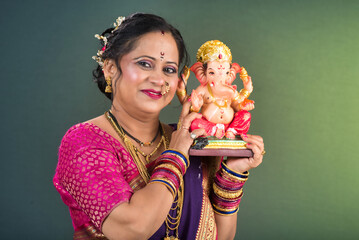 Happy traditional Indian woman wearing saree holding and posing with Ganesha statue on the occasion...