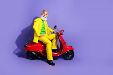 Photo of cheerful extravagant senior man wearing yellow trendy costume sitting moped isolated on purple color background