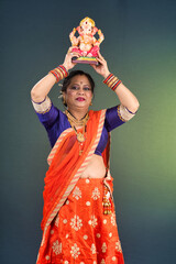 Happy traditional Indian woman wearing saree holding and posing with Ganesha statue on the occasion of Ganesh Festival