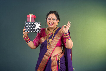 Happy traditional Indian woman wearing saree holding and posing with gift box