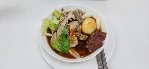 Delicious rolled Rice Noodles in Five-spices Broth or boiled Chinese pasta square with pork in brown soup, pork entrails, pork blood, boiled eggs, lettuce, with pickled chili peppers for extra flavor
