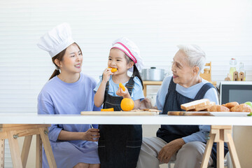 cute little girl eating orange beside mother and grandmother in the kitchen