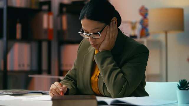 Focused Asian female teacher grading students written assignments in class