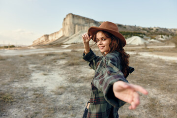 Woman in plaid shirt and hat standing in front of majestic mountain landscape