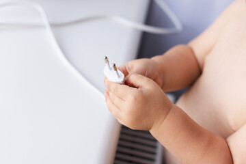 Little child holding power plug. Dangerous situation.