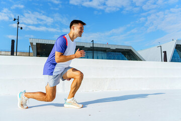 A man in athletic gear performs a lunge exercise outdoors, showing focus and strength under a clear blue sky.