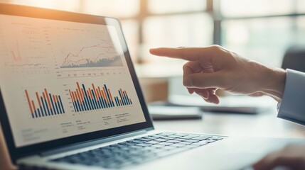 A hand pointing at an analytical graph displayed on a laptop screen in a sunlit office setting, demonstrating the business analysis and strategy review process.