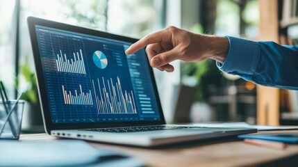Image showing a hand pointing at a laptop screen displaying colorful charts and graphs, representing data analysis and collaborative work in a vibrant office setting.