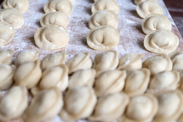 The raw dumplings were placed on a wooden cooking board, sprinkled with flour. The filling is minced meat, potatoes, cheese or cottage cheese. A semi-finished product, ready for cooking.