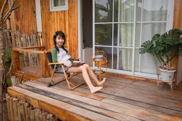 a girl sits on a porch outside with a chair and a window