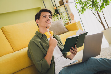 Photo of young man sitting carpet working from home using modern device living room interior home...