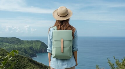 Fototapeta premium Woman Traveler with Backpack Admiring Ocean View - A woman wearing a hat and a backpack stands on a hilltop overlooking a beautiful ocean view, symbolizing adventure, exploration, travel, freedom, and