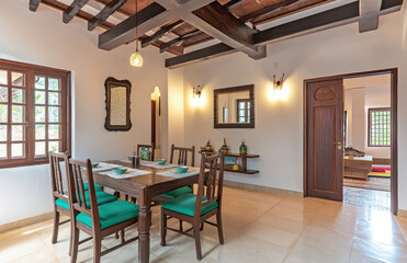 A photograph of an Indian dining room with a wooden table and chairs, white walls, green accents on the furniture. Created with AI