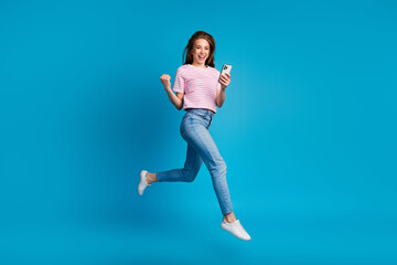 Full body photo of attractive young woman running jump winning hold device dressed striped pink...