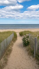 Obraz premium A tranquil pathway of wooden planks leads through lush dunes and vibrant pink roses to the calm ocean, with a clear sky and soft white clouds overhead