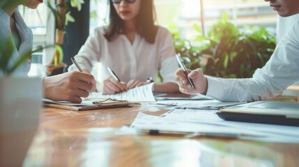 A close-up of a group of people collaborating on paperwork at a table filled with documents, pens, and laptops, highlighting teamwork and productivity.