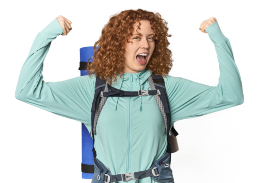 Young Caucasian redhead ready for hiking showing strength gesture with arms, symbol of feminine power