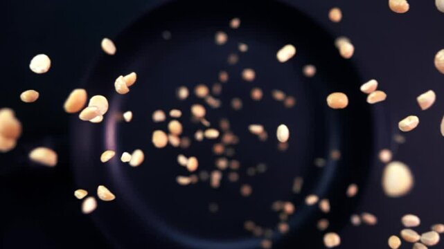 Super slow motion of rotating roasted peanuts falling onto a frying pan