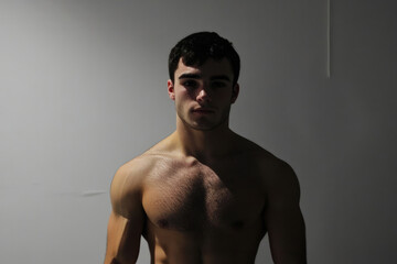 A bodybuilder with a muscular and fit physique poses shirtless against a dark backdrop, showcasing their well-defined muscles and dedicated fitness journey.