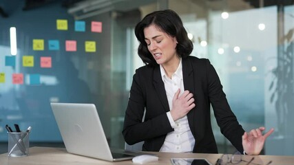 Businesswoman in office feeling sudden chest pain while using laptop. Concern, potential heart attack symptoms. Stress, health issues urgency. Sick female worker is breathing deeply needs medical help