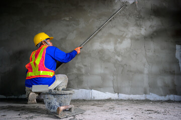 Back view of a male construction worker using a trowel and cement to plaster a house wall A worker is plastering a gray wall in a room where a new house is being built.